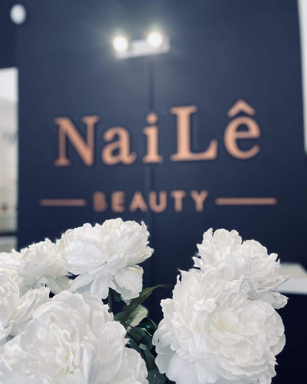 The NaiLê Beauty sign on the back wall behind white peonies