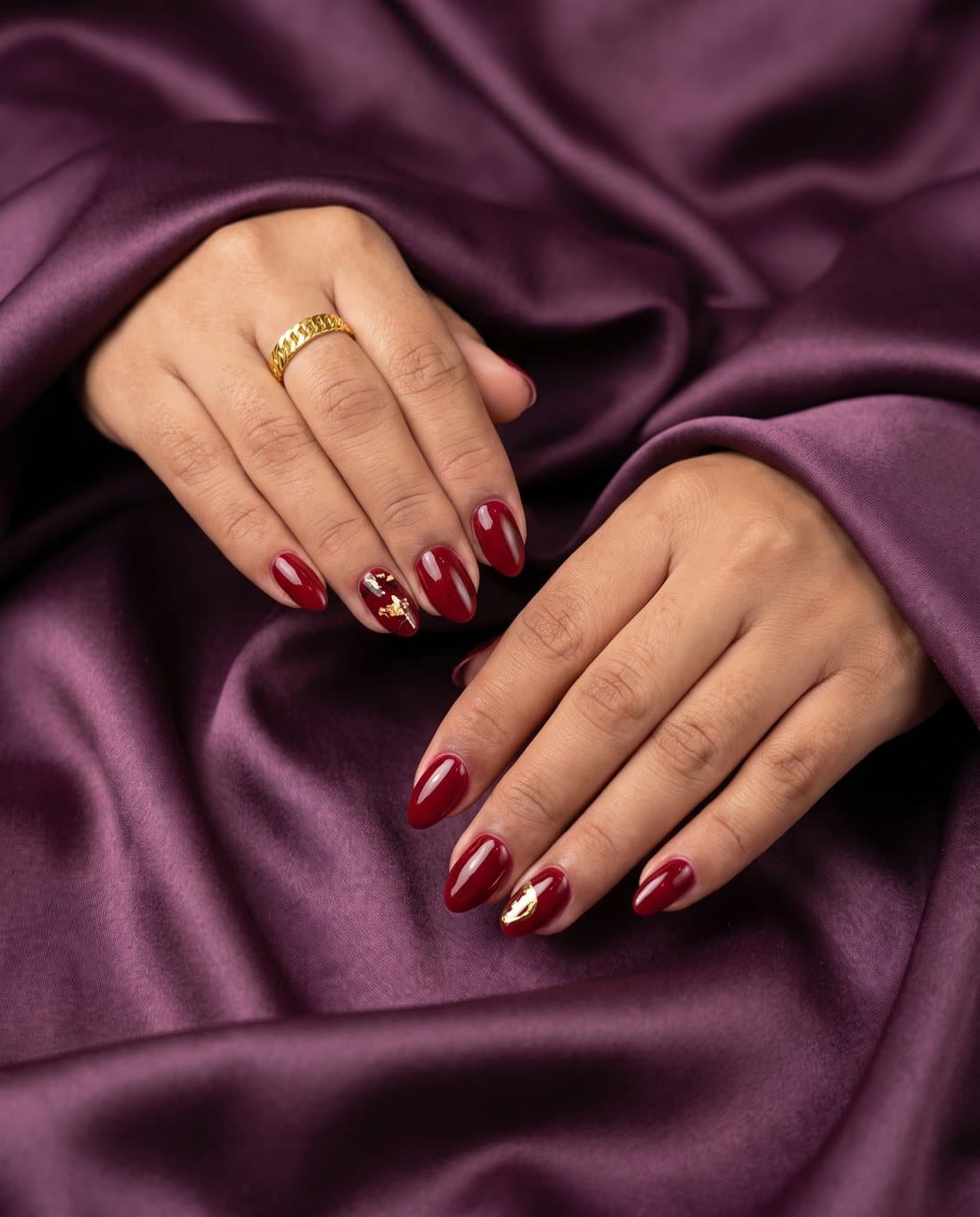 Deep red almond nails with a gold foil accent